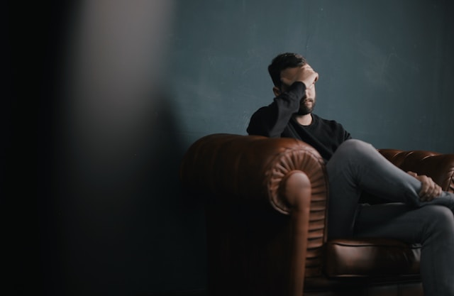 photo of a man sitting on a leather chair with his head resting in his hand