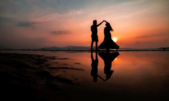 photo of a man twirling a woman on the ocean at sunset