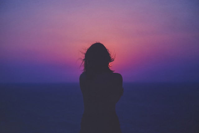 silhouette of a woman looking out at a sunset sky
