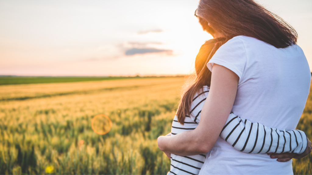 mother hugs daughter and in the background there is a flower-filled field.